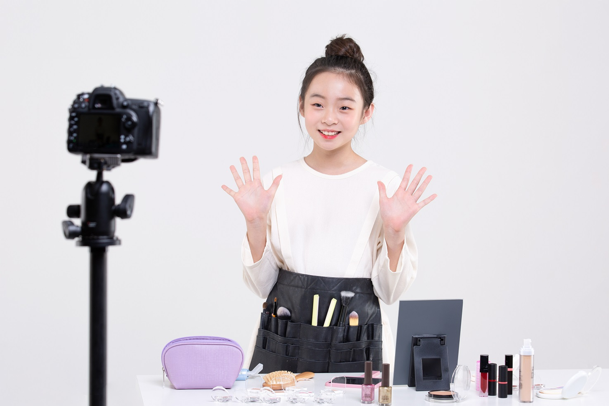 一名女性錄製美妝影片，用化妝工具展示化妝技術，背景是一臺攝影機和美妝產品。