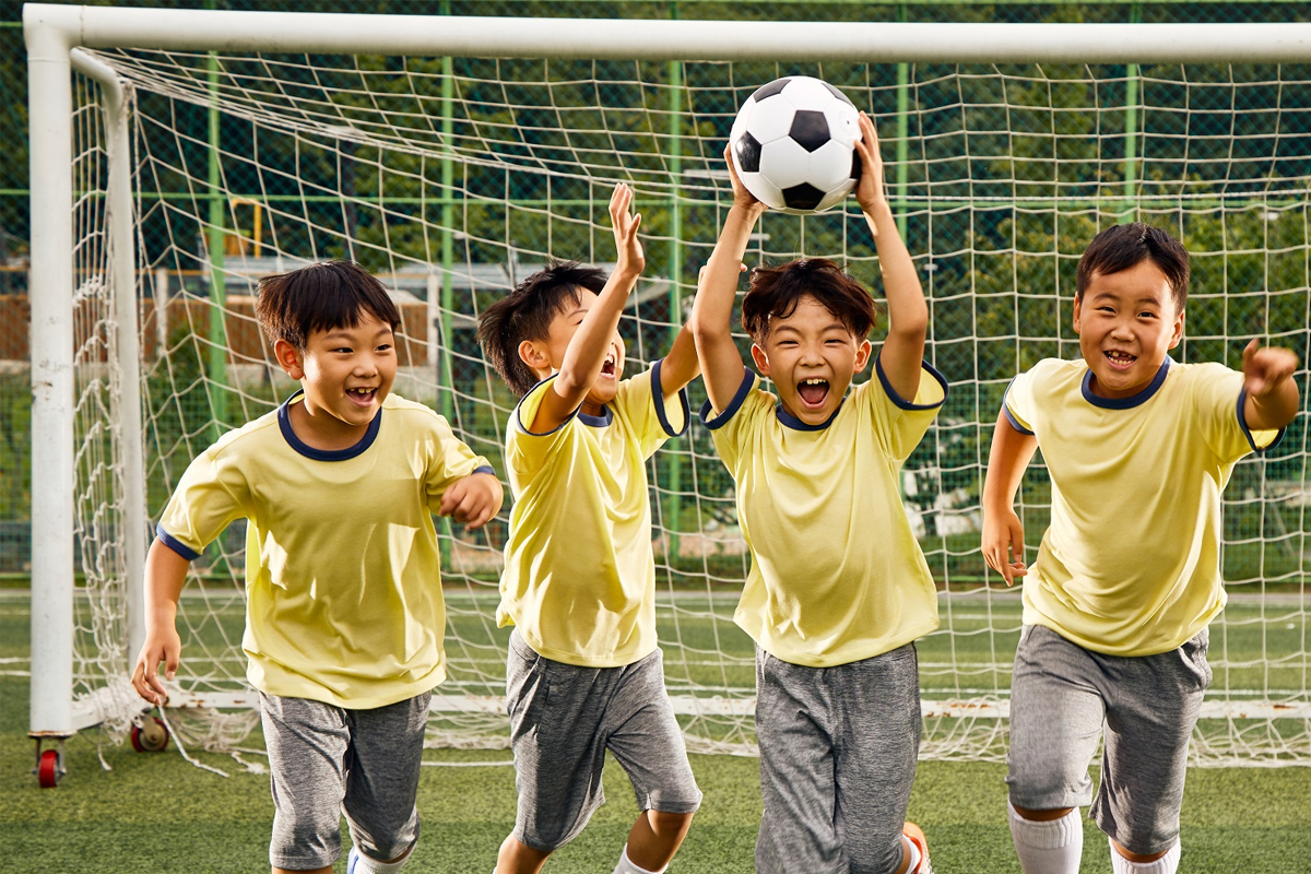 一群穿著黃色球衣的韓國小學生在足球比賽中奔跑，背景是一個足球門。