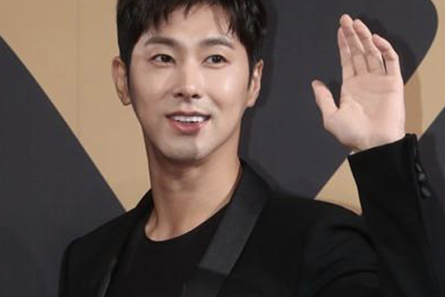 東方神起成員允浩在活動中舉手致意，背景為活動海報