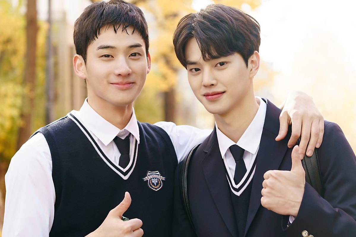 兩名身穿制服的韓國男學生站在學校走廊中，互相搭肩微笑