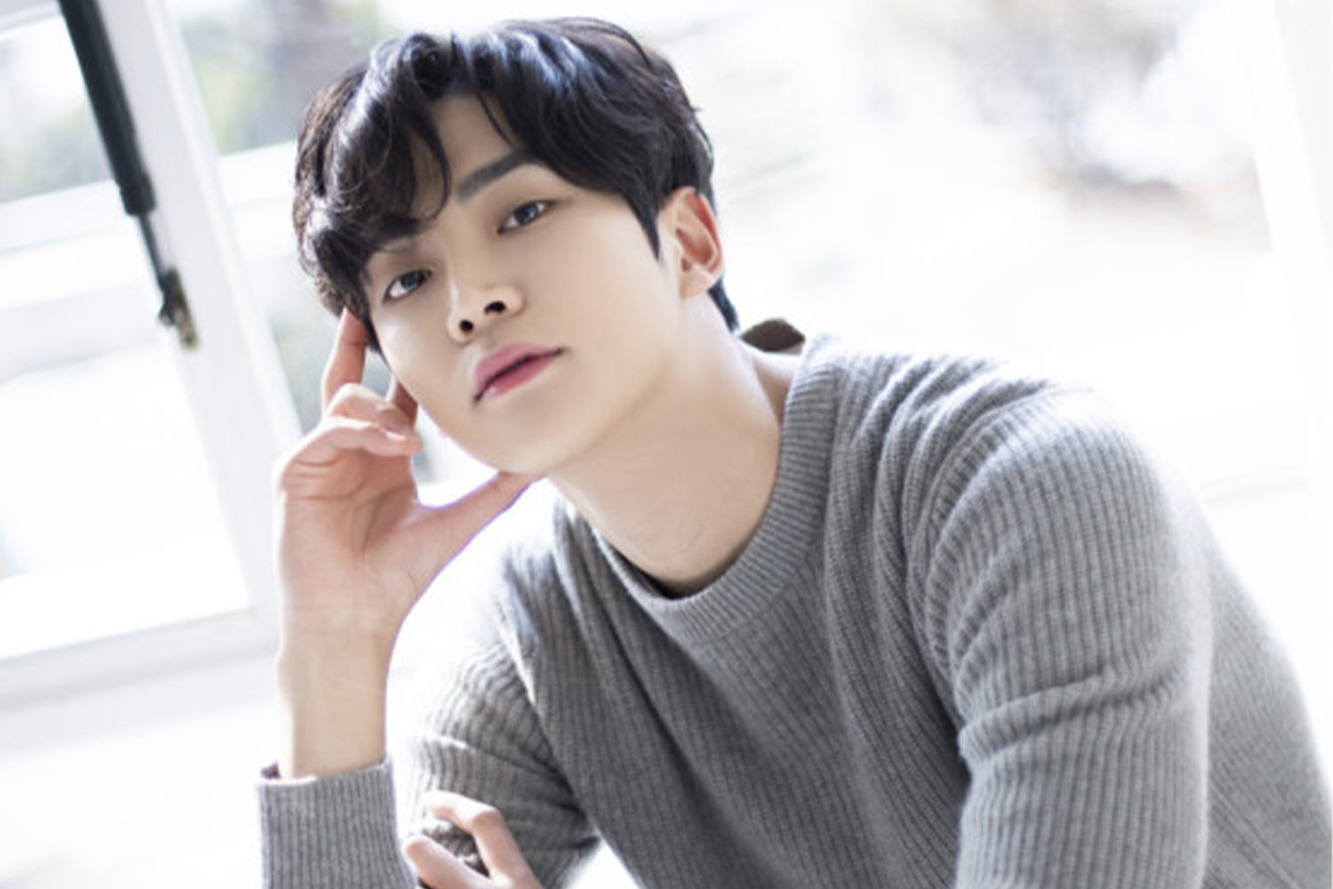 SF9成員路雲坐在窗前，身穿灰色針織毛衣，手靠在下巴上，模特般的姿勢。