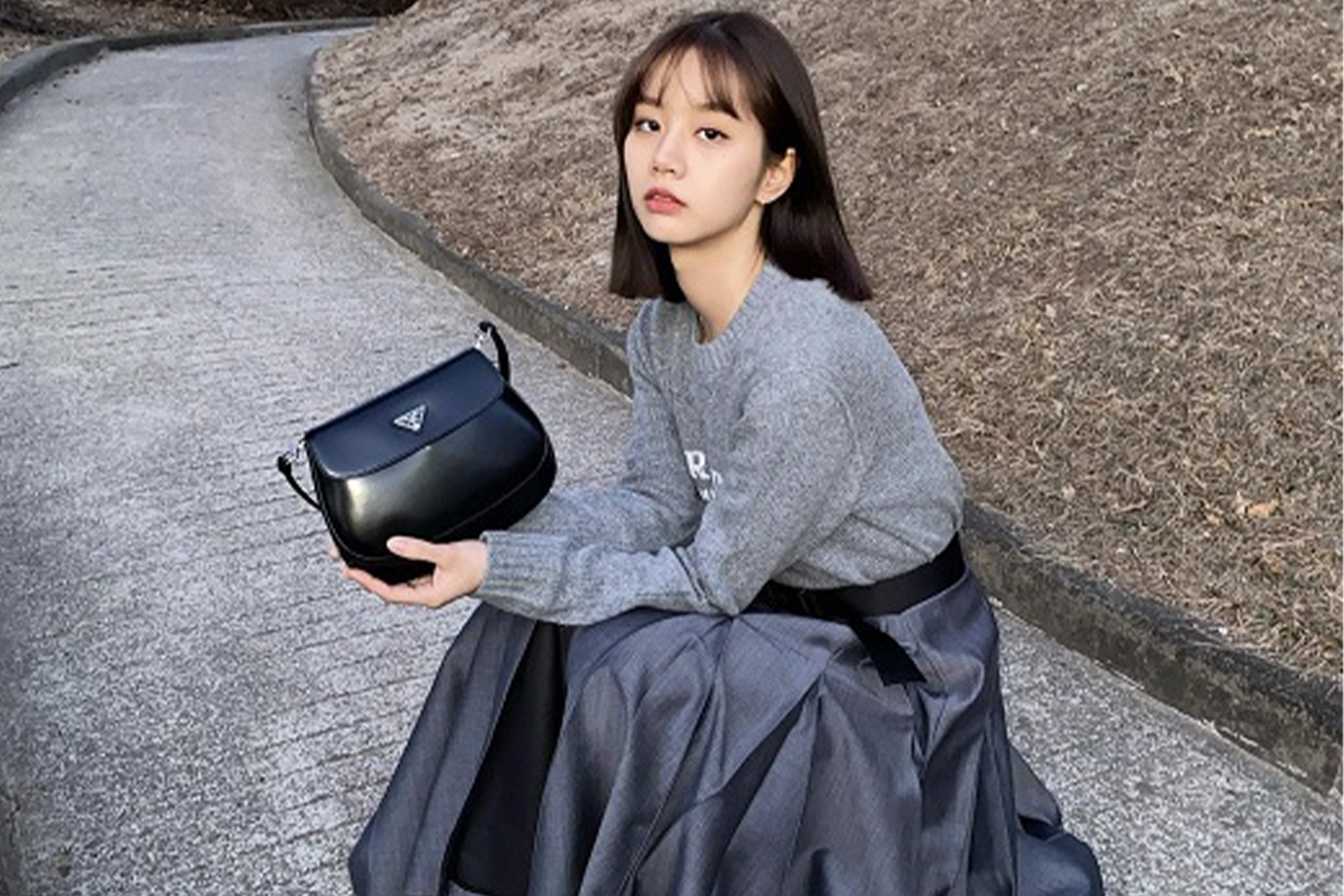 Girl's Day惠利坐在户外，身穿灰色針織毛衣，手拿着黑色Prada包包，周圍是冬日的景色。