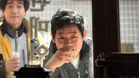 Một người Hàn Quốc đang thực hiện động tác rủ bạn bè đi uống rượu bằng cách tay giả vờ cầm chén rượu và uống, mang đậm nét văn hóa đặc trưng.