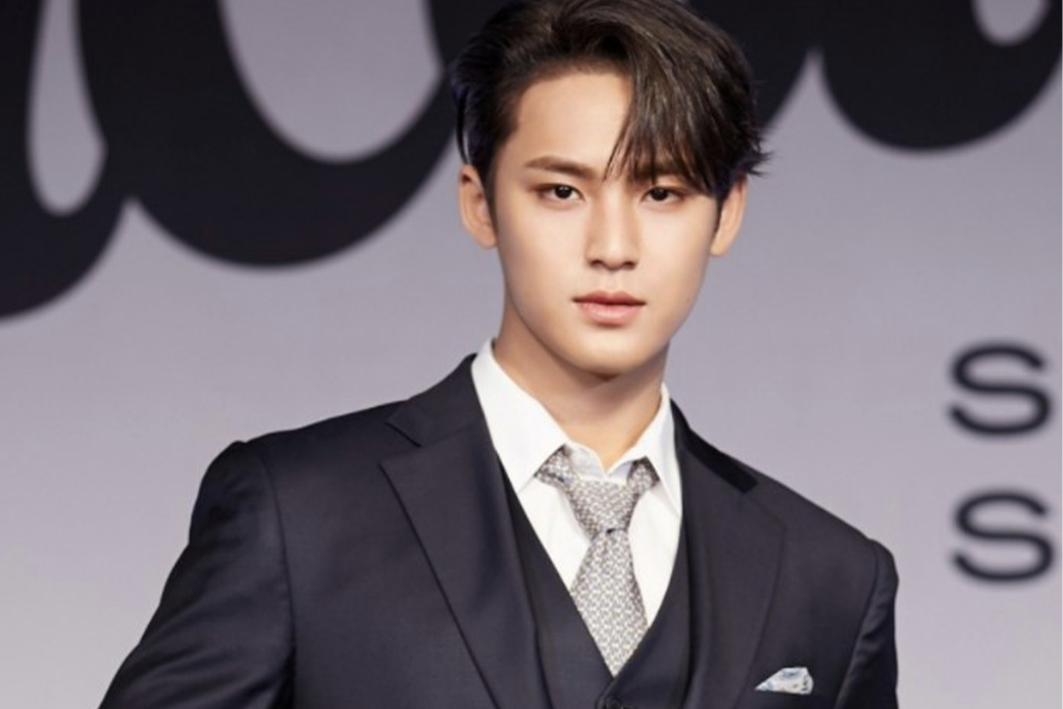 身穿黑色西裝的男子在活動現場，背景為活動標誌。