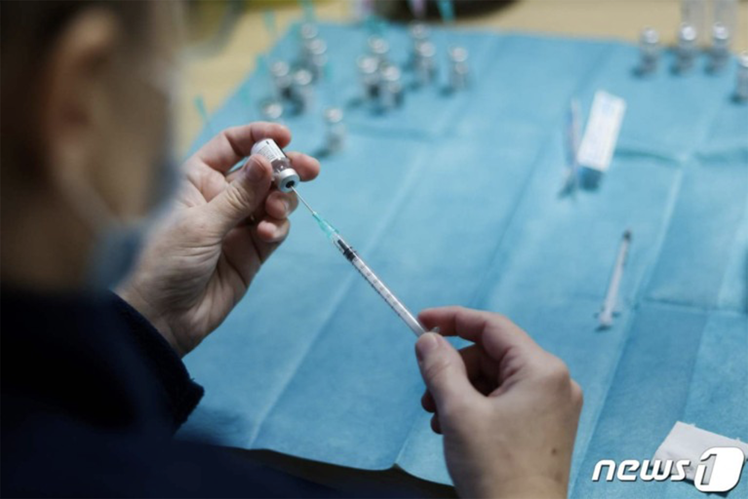 醫護人員準備新冠疫苗注射，一名手持疫苗瓶及注射器的工作人員，背景有其他未使用的疫苗器材放在藍色布上。出處：NEWS1