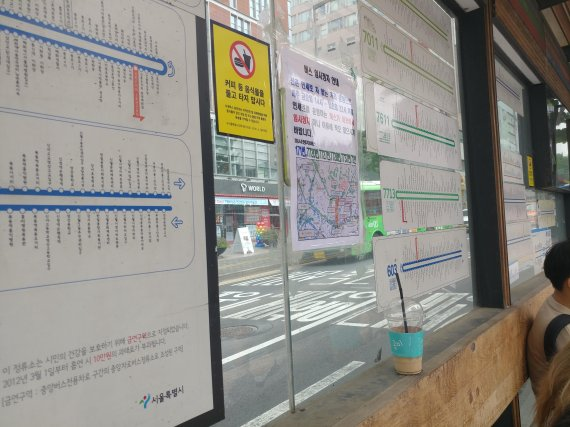 ソウルのバス停での待機中の様子。バス停には路線案内が表示されており、通りを見下ろす位置からの写真。コーヒーカップが棚に置かれているのがわかる。