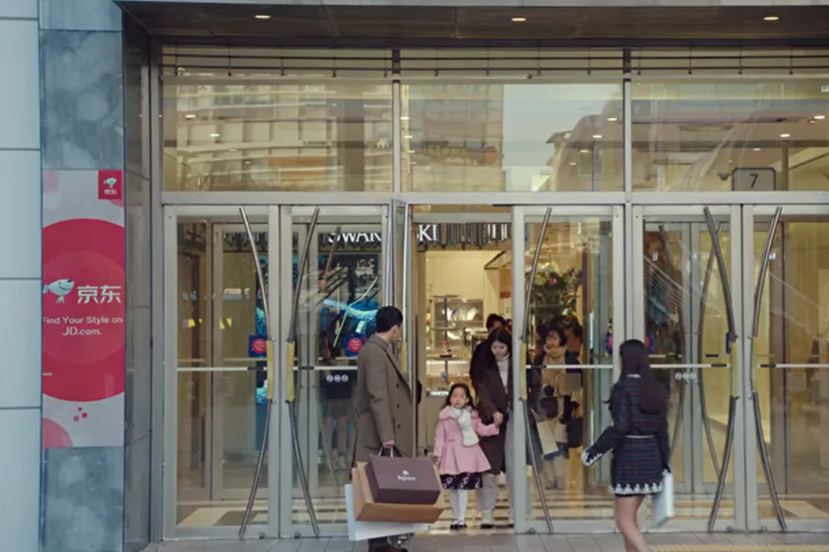 kdrama crash landing on you scene with hyun bin holding open mall door with chinese brand banner hanging on side