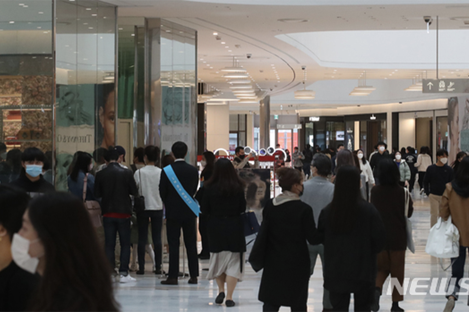首爾某商場內人羣排隊以進行新冠病毒防疫措施，部分人佩戴口罩，畫面展示防疫政策的實施情況。