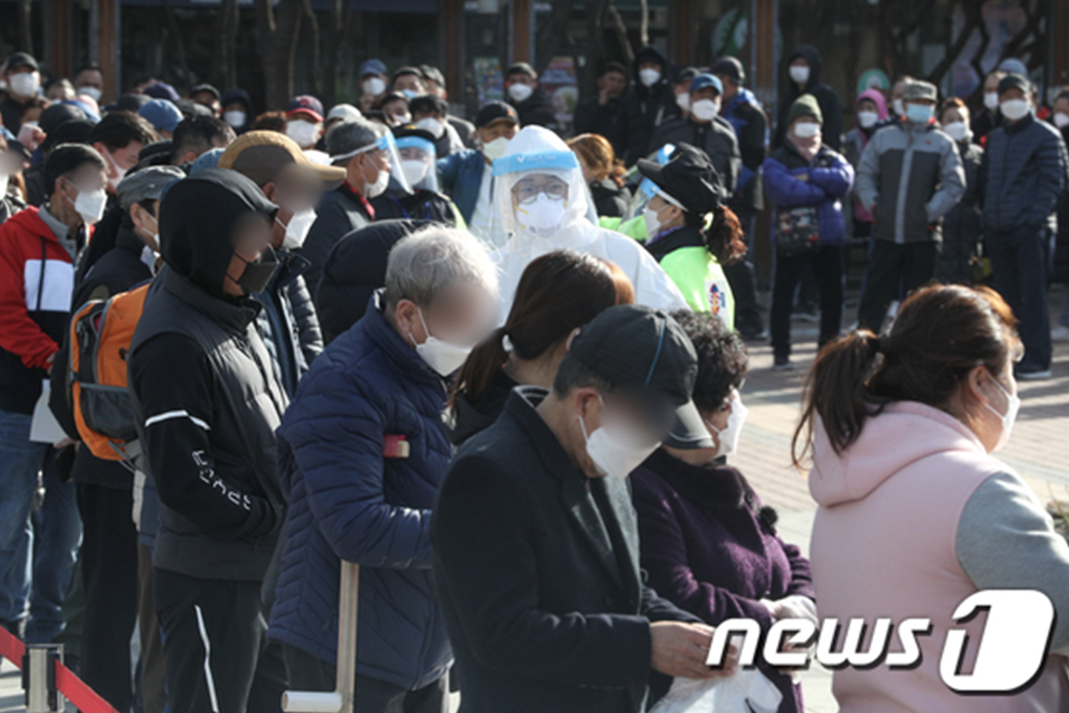 在韓國首爾一處室外空間，人羣排隊等待進行新冠病毒檢測，現場有防疫工作人員協助維持秩序，羣眾佩戴口罩。