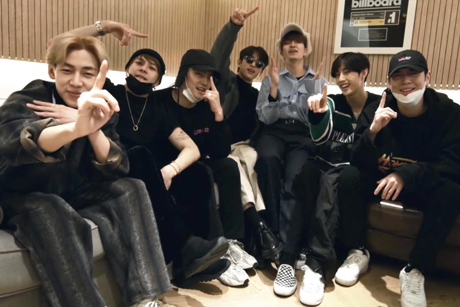 สมาชิก GOT7 นั่งรวมตัวกันบนโซฟาในห้องที่มีบรรยากาศสบาย ขณะที่สมาชิกชูนิ้วหัวแม่มือและชี้นิ้วในท่าทางที่เป็นเอกลักษณ์ พื้นหลังมีแผ่นประกาศรางวัลจาก Billboard