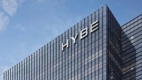 HYBE本社ビル外観、大きな窓ガラスで覆われた近代的なデザイン、頂上にHYBEのロゴが表示されている。