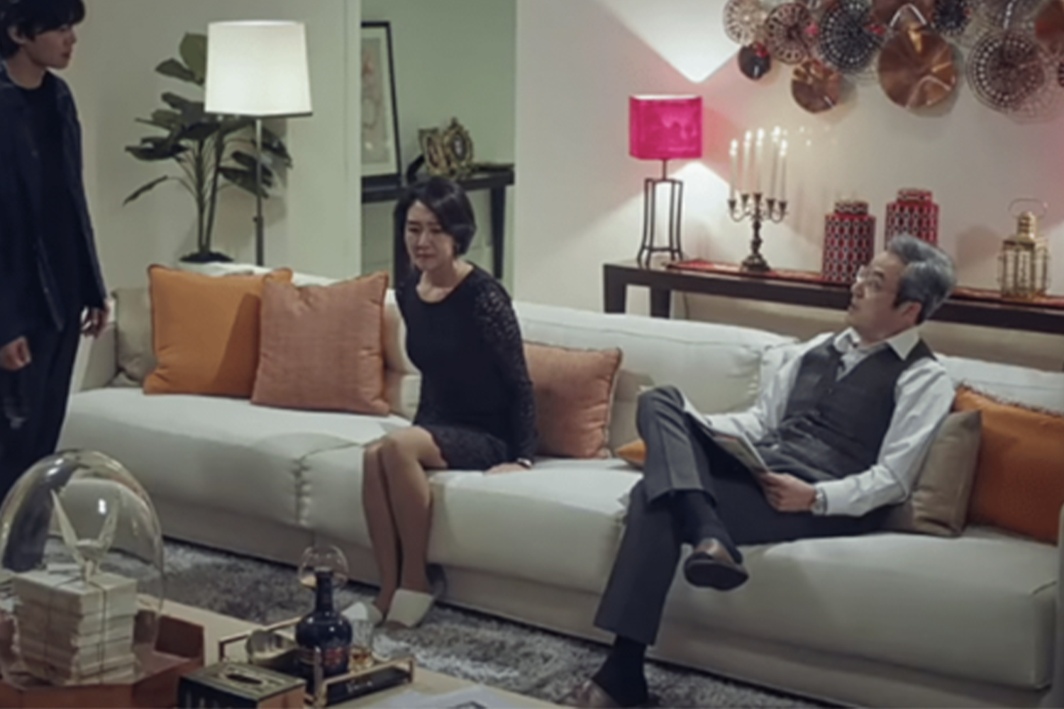 羅根爸爸穿著正式西裝，坐在背景簡潔的場所，象徵其在商業界的超級富豪身份。