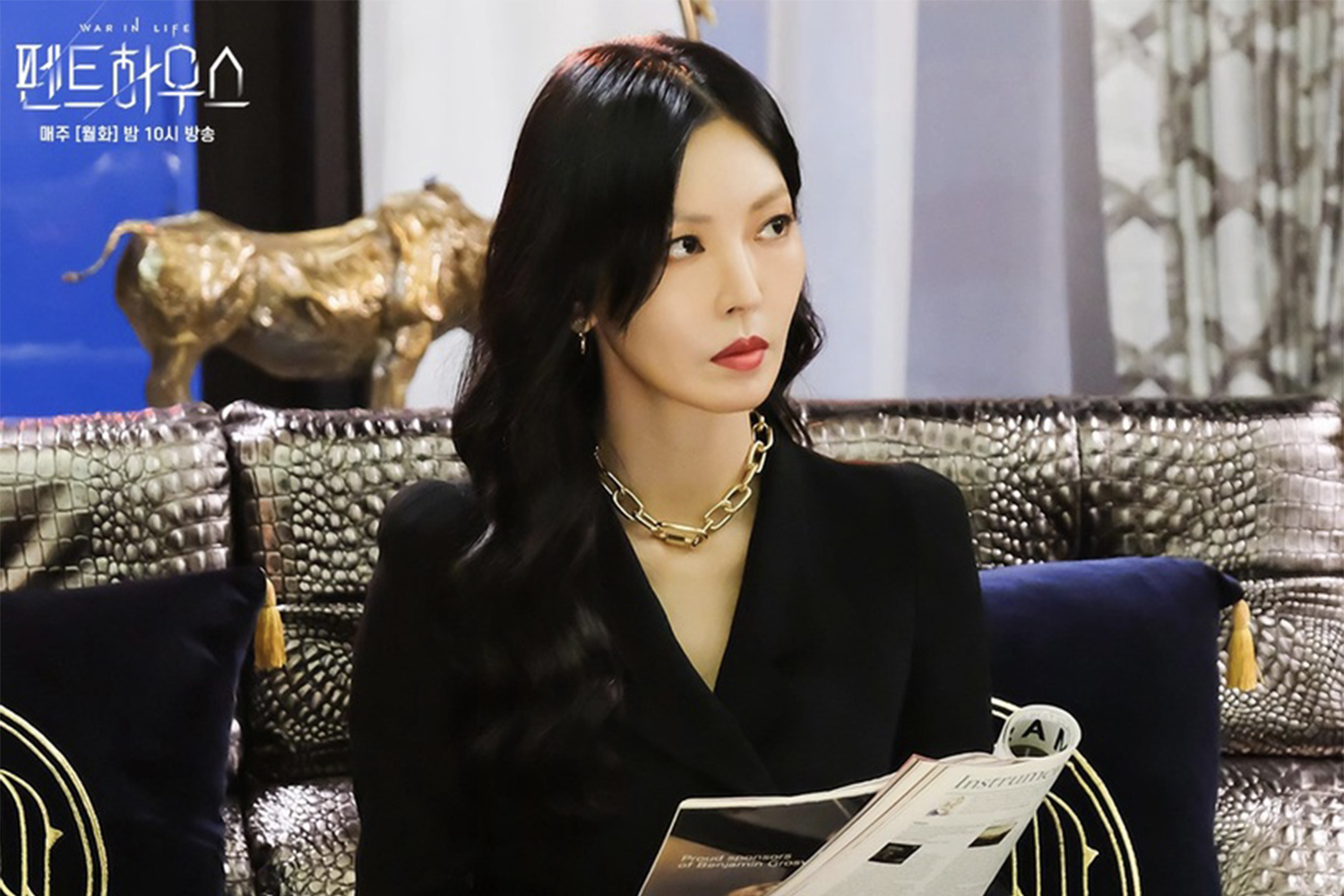 千書真穿著灰色外套和黑色襯衫，坐在居家環境，背景是室內植物和現代藝術品。