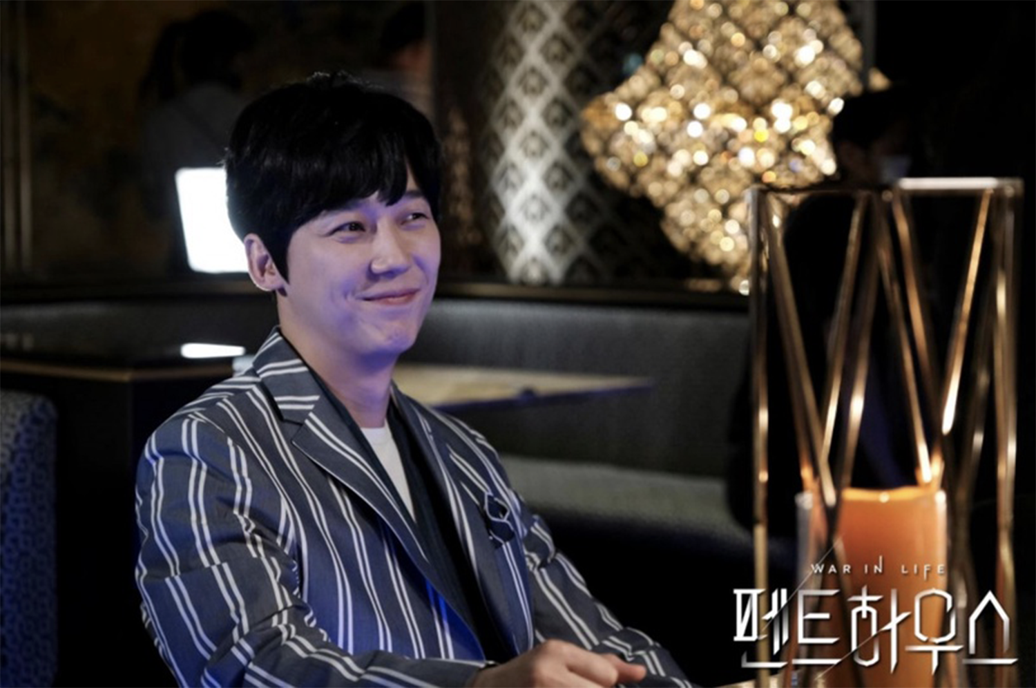 河允徹穿著條紋西裝，坐在赫拉皇宮的酒吧內，背景有現代裝飾燈光。