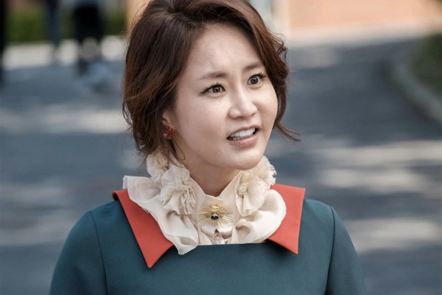 姜瑪莉穿著華麗的紅色和白色襯衫，站在室外走道。