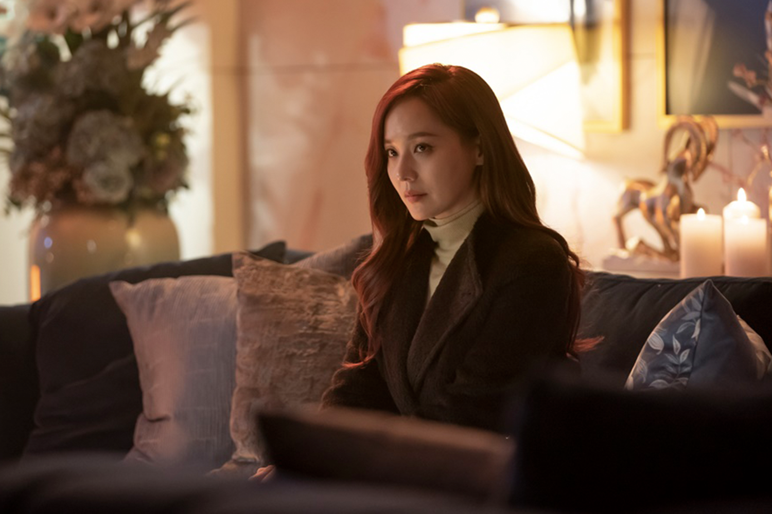 吳允熙坐在赫拉皇宮的沙發上，穿著深色外套，背景有花瓶和燈光。