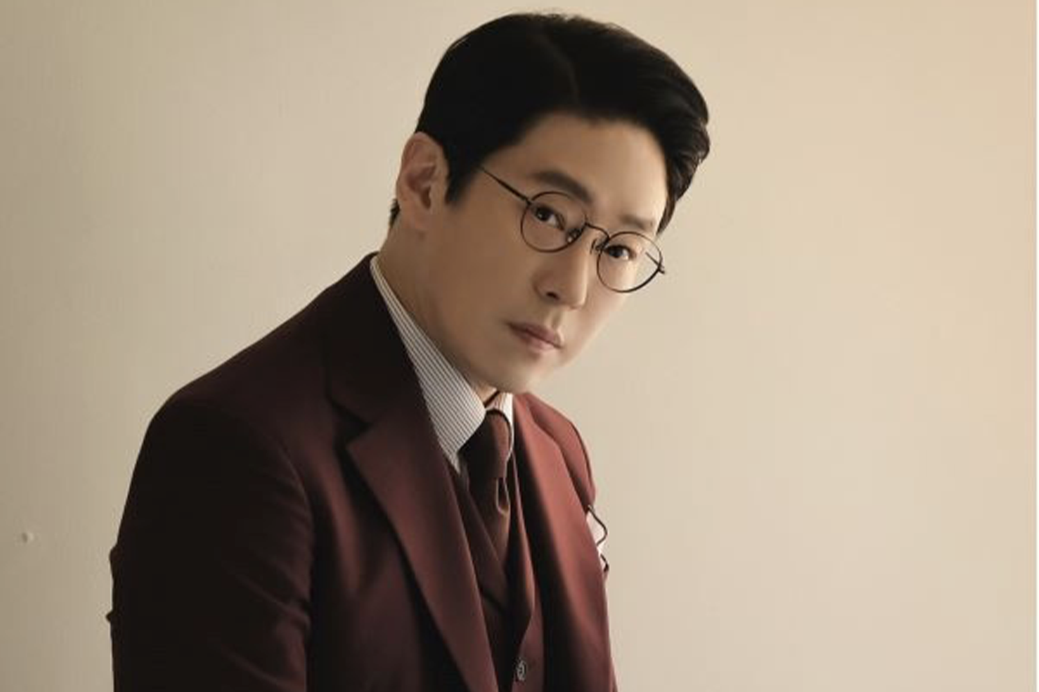 朱丹泰穿著紅色西裝，站在淺色牆前，展現他在韓國建築業的身份。