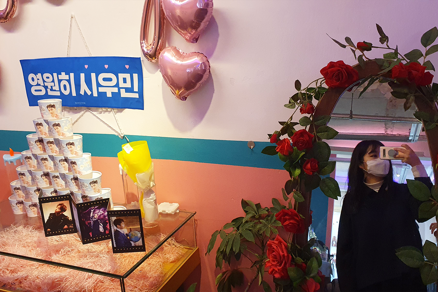 카페 내 전신 거울에서 XIUMIN의 사진을 배경으로 포즈를 취하는 사람의 모습.