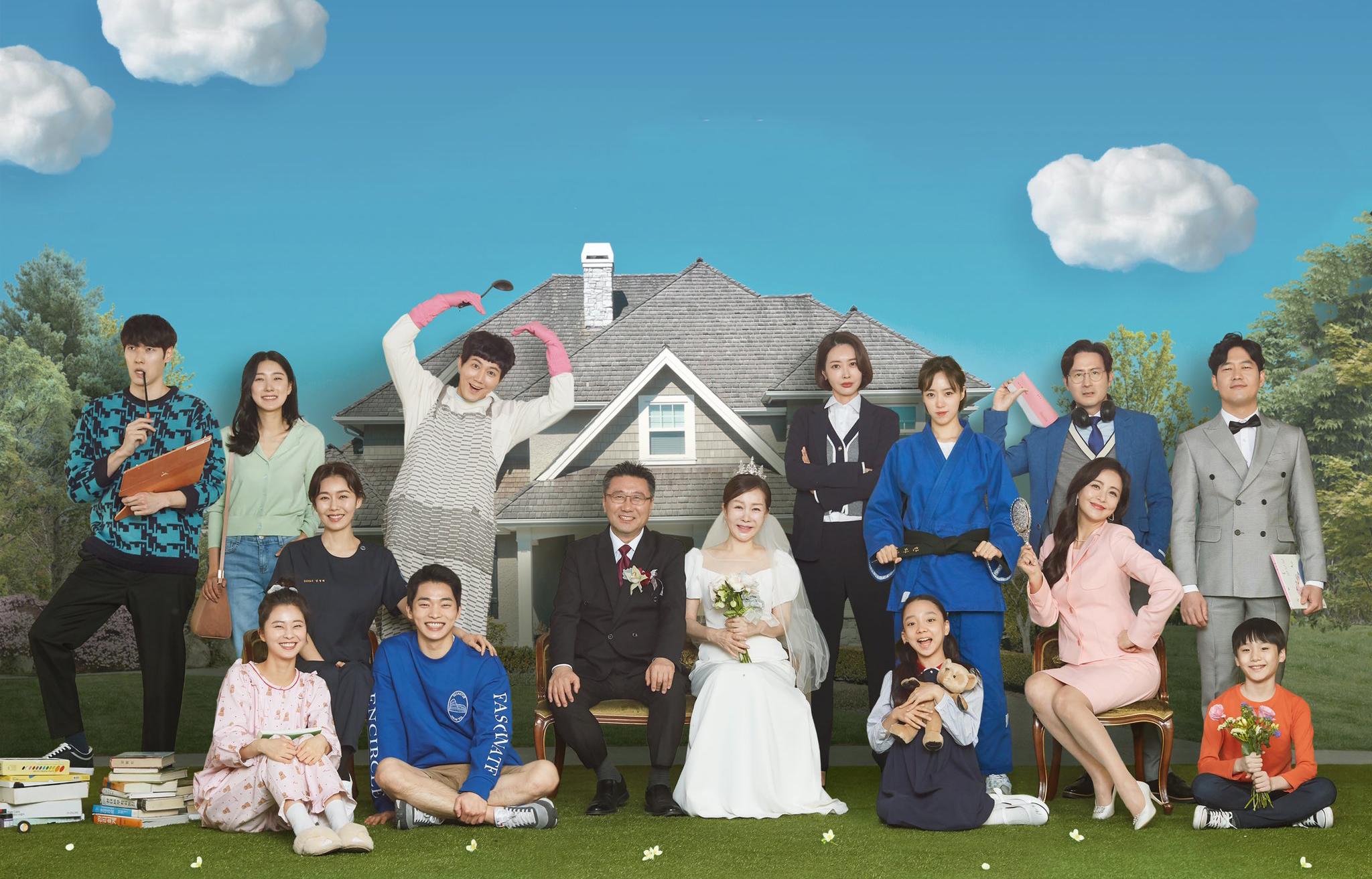 ครอบครัวที่มีสมาชิกหลากหลายยืนและนั่งอยู่ร่วมกันหน้าบ้านสองชั้น พร้อมสวมเสื้อหลากสีแสดงให้เห็นถึงความมีชีวิตชีวาและความสัมพันธ์ของครอบครัว