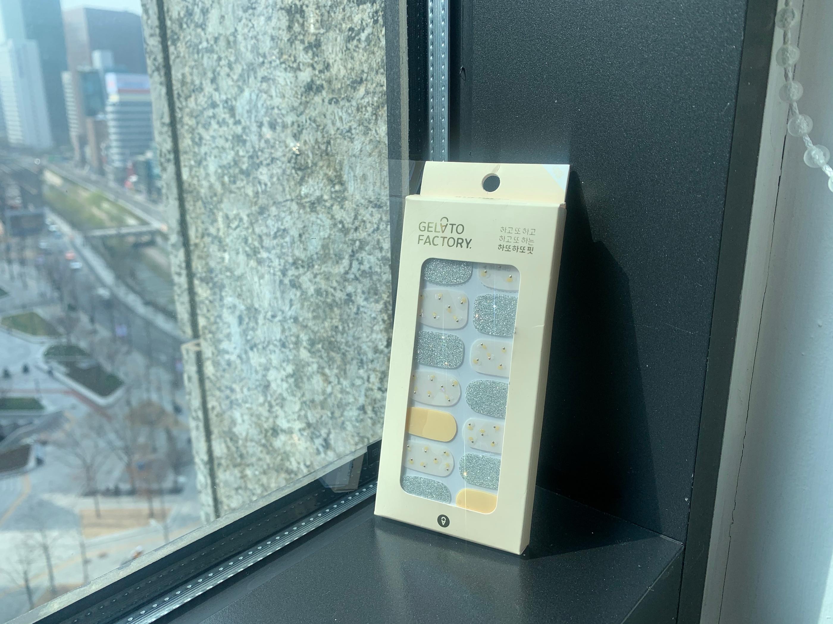 Gelato Factory Nagelsticker in Gelb, Silber Glitzer und blumenähnlichem Muster auf Fensterbank gestützt