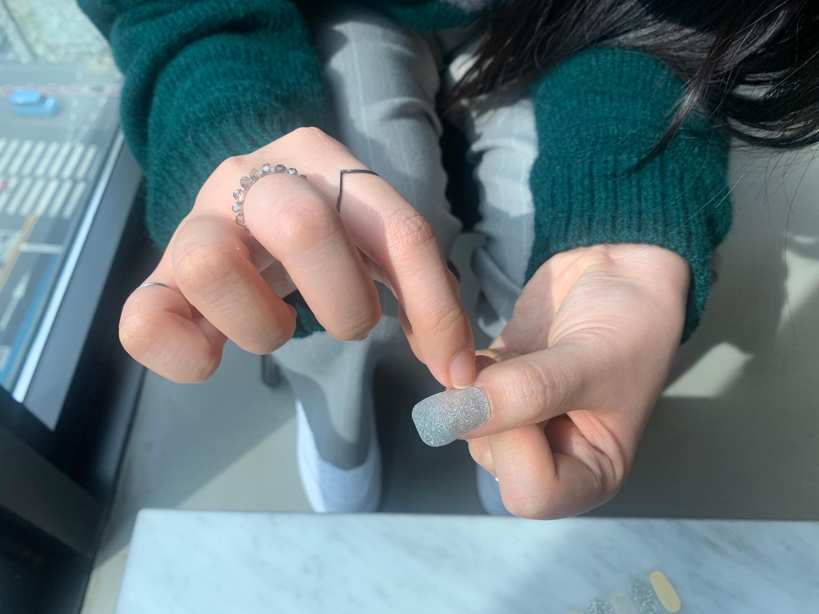 pressing down silver glitter nail sticker down into cuticle