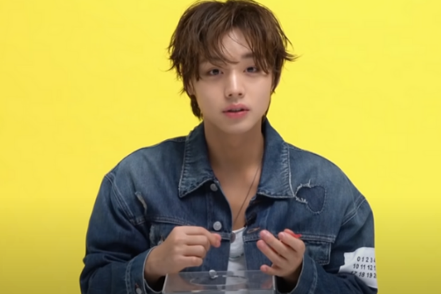 韓國雜誌 GQ Korea 的訪談中穿著牛仔夾克的名人手握透明盒子,背景為黃色