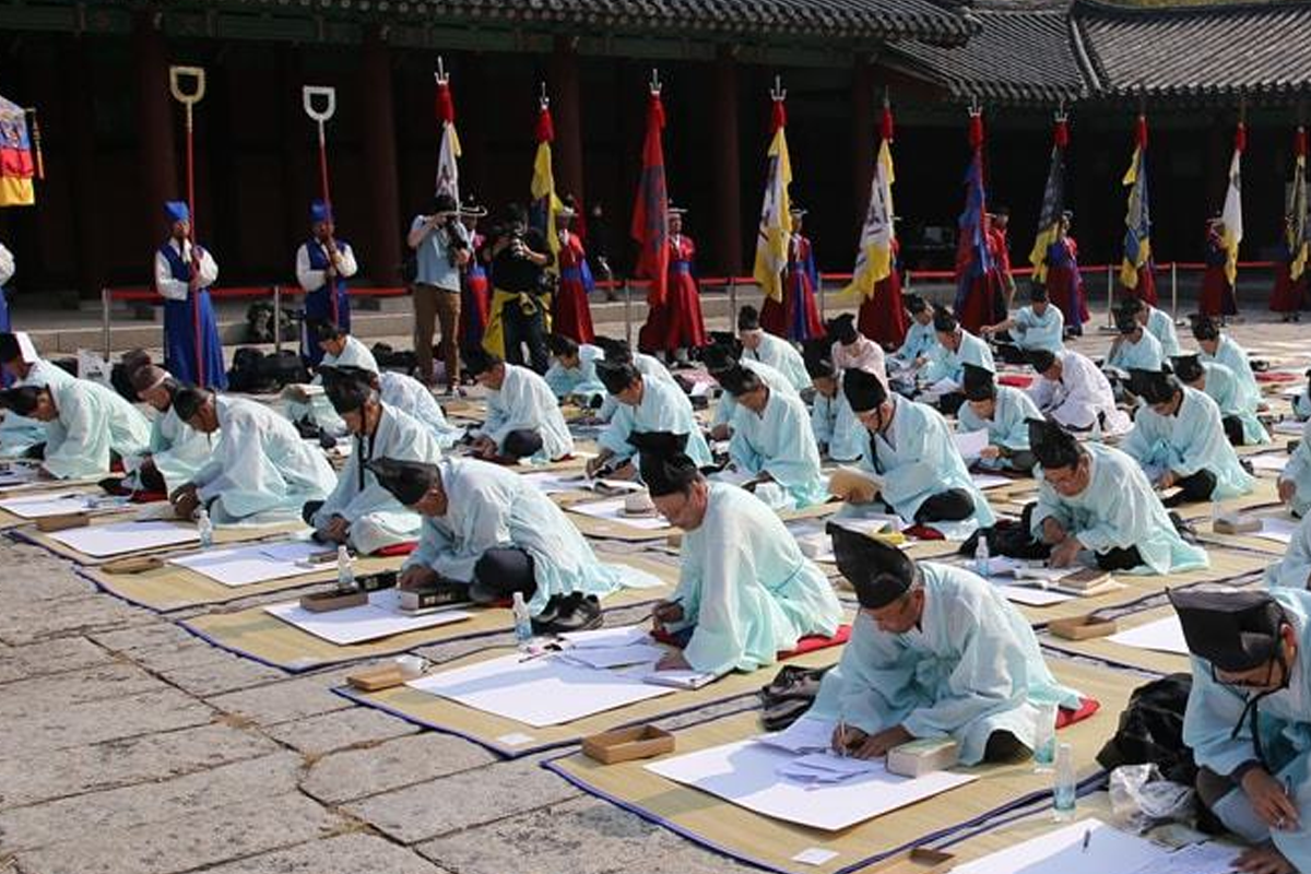 考生们身穿青色传统汉服，在考试现场席地而坐，认真写作，背景是丰富的传统文化元素。