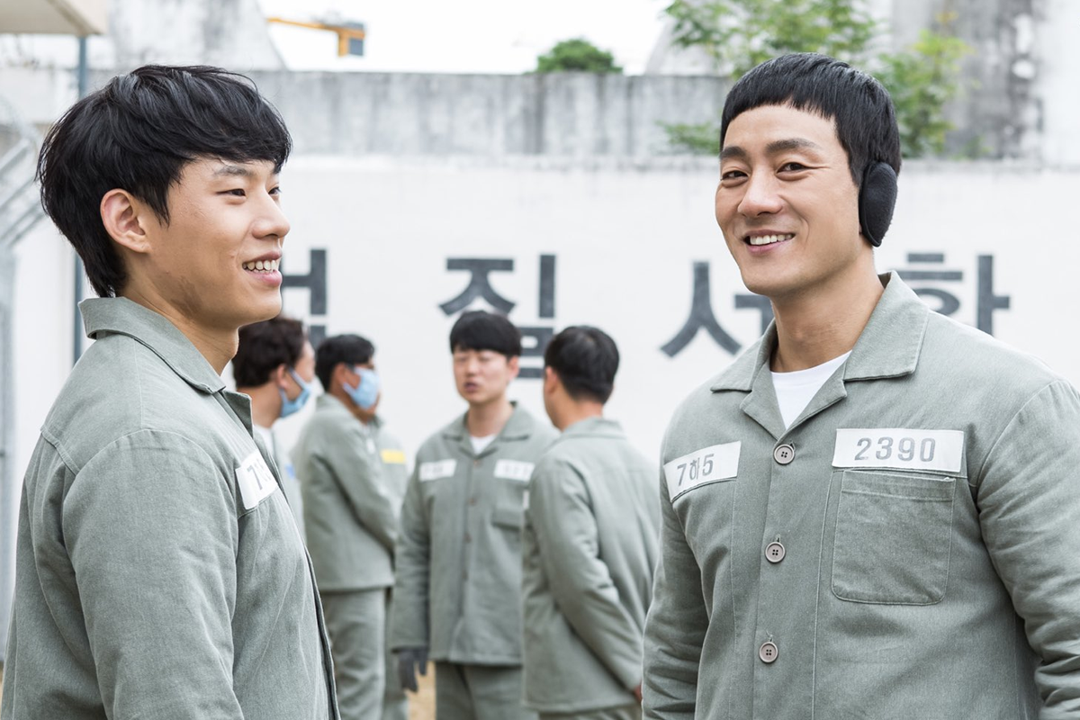 韩剧《机智牢房生活》剧照，穿监狱服的人物在户外，墙壁上有韩文标识