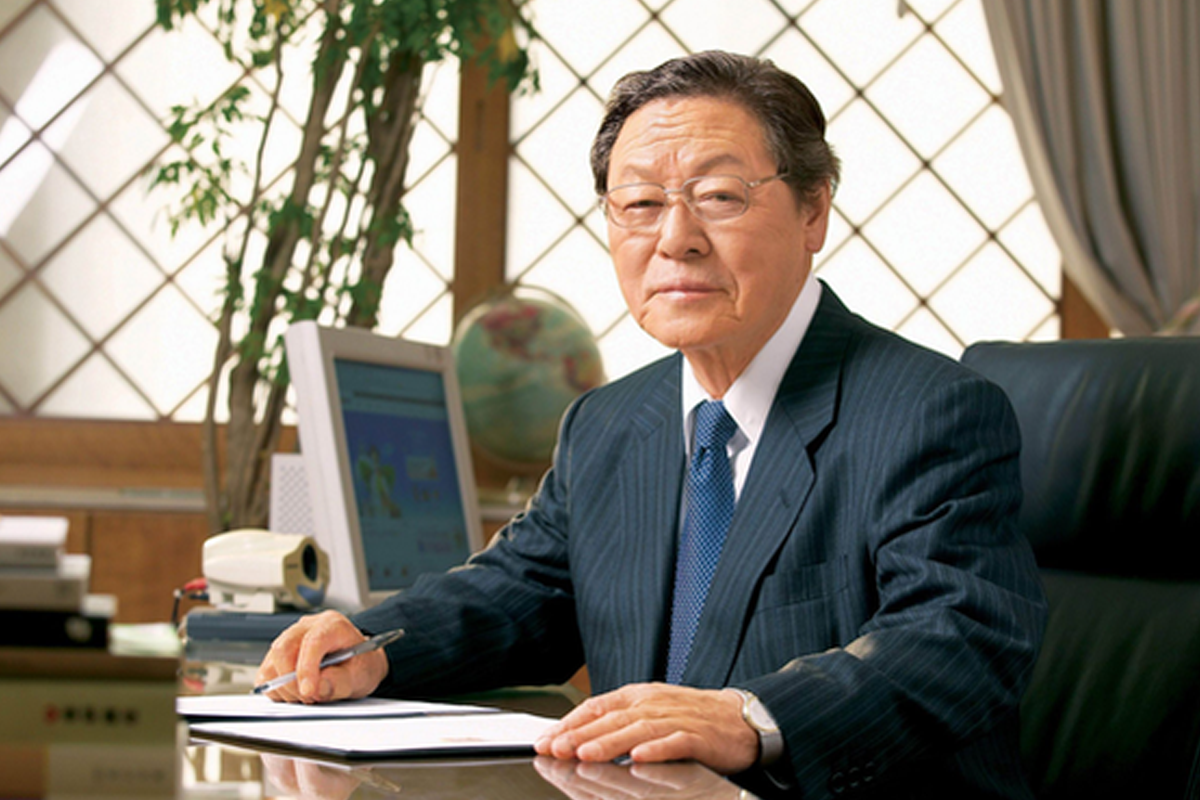 辛春浩正在辦公室工作，坐在桌前寫字，背景中有地球儀和電腦顯示器。