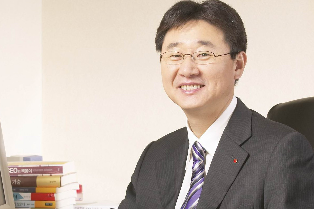 辛東原坐在桌前工作，背景中有整齊排列的書籍和一臺電腦。