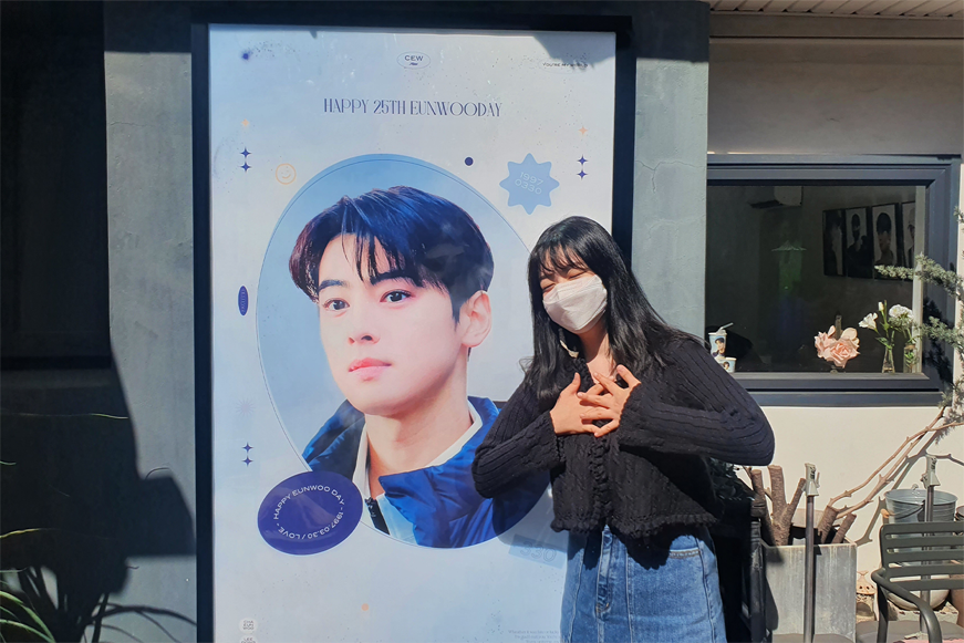 一位身著深色衣服的女性站在大幅海報前微笑，突顯咖啡廳的慶祝氛圍。