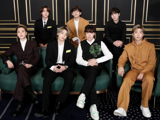 BTSメンバーがフォーマルなスーツを着てソファに座っている写真。メンバーはさまざまな色のスーツを着用し、エンタメ業界のイベントで和やかに写真撮影をしている様子。