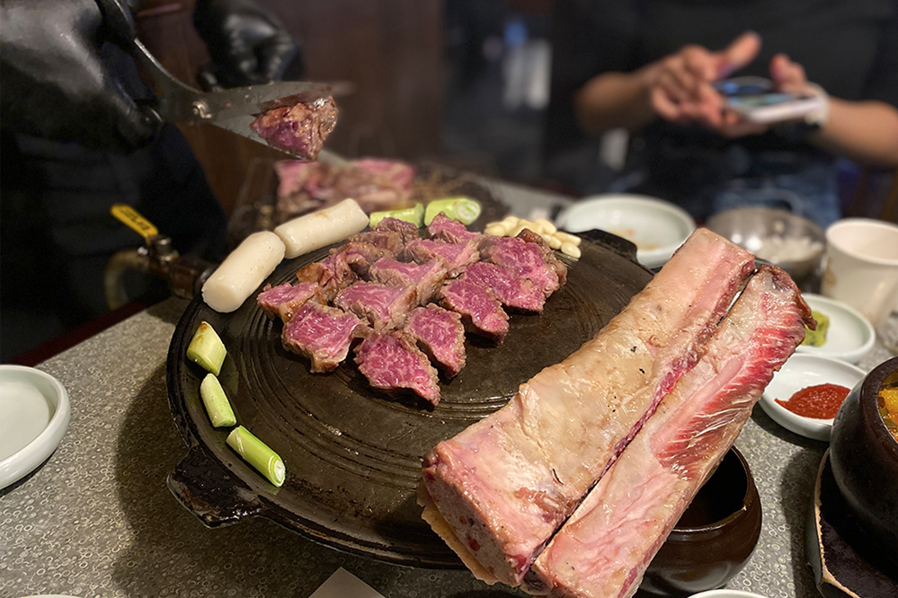 位於韓國首爾的夢炭餐廳，牛大排骨正被烹製，其上炭烤與準備中切片，展示令人垂涎的烹飪技藝與肉品的誘惑。