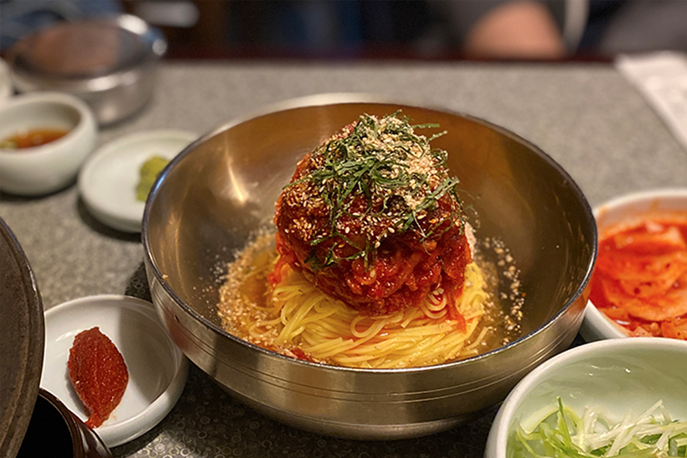 韓國首爾梨泰院夢炭餐廳的招牌冷麵，展示著豐富的配料與麵條盛在金屬碗中，為顧客提供完美的搭配選擇。讓人胃口大開的韓國美食。