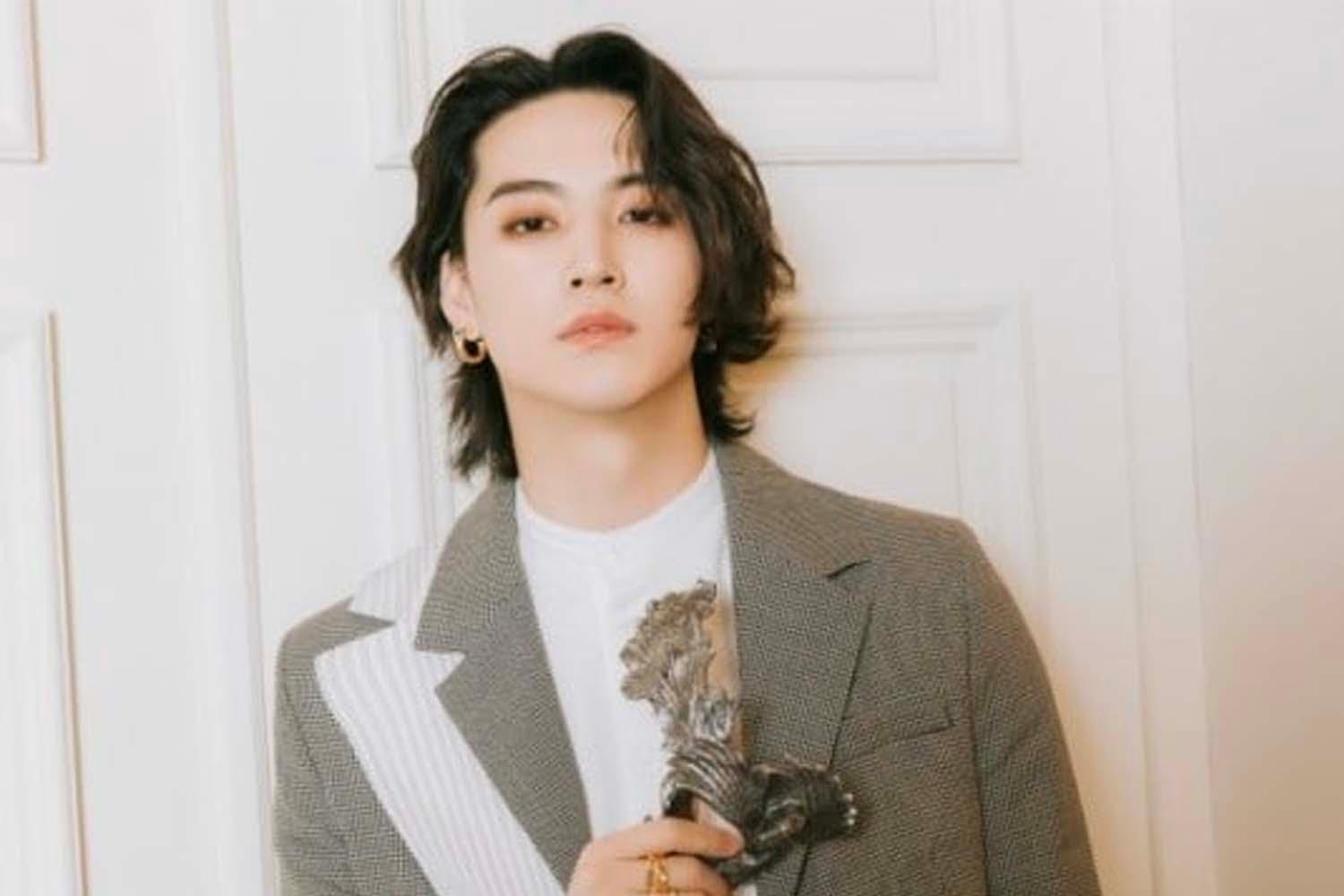 เจบี GOT7 สวมเสื้อสูทสีเทา ถือไอเทมแฟชั่นที่โดดเด่น ด้วยพื้นหลังสีขาวตัดกับประตูที่มีกรอบด้านหลัง