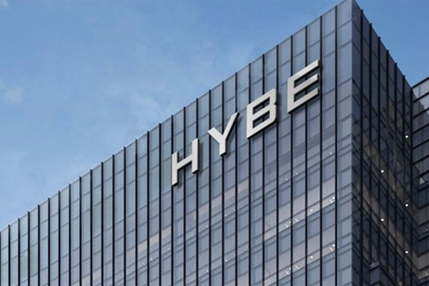 **透明大廈上的HYBE標誌**: 位於韓國首爾的HYBE公司總部，代表著其Global影響力和娛樂行業的最新收購策略。