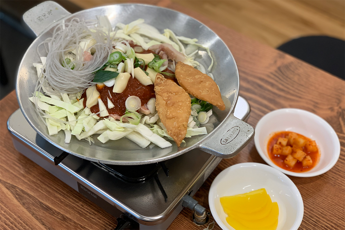 正正在煮緊嘅梨大火飯，充滿多樣化嘅食材，包含韓式炸物、冬粉、以及多種蔬菜，提供豐富口感與營養。