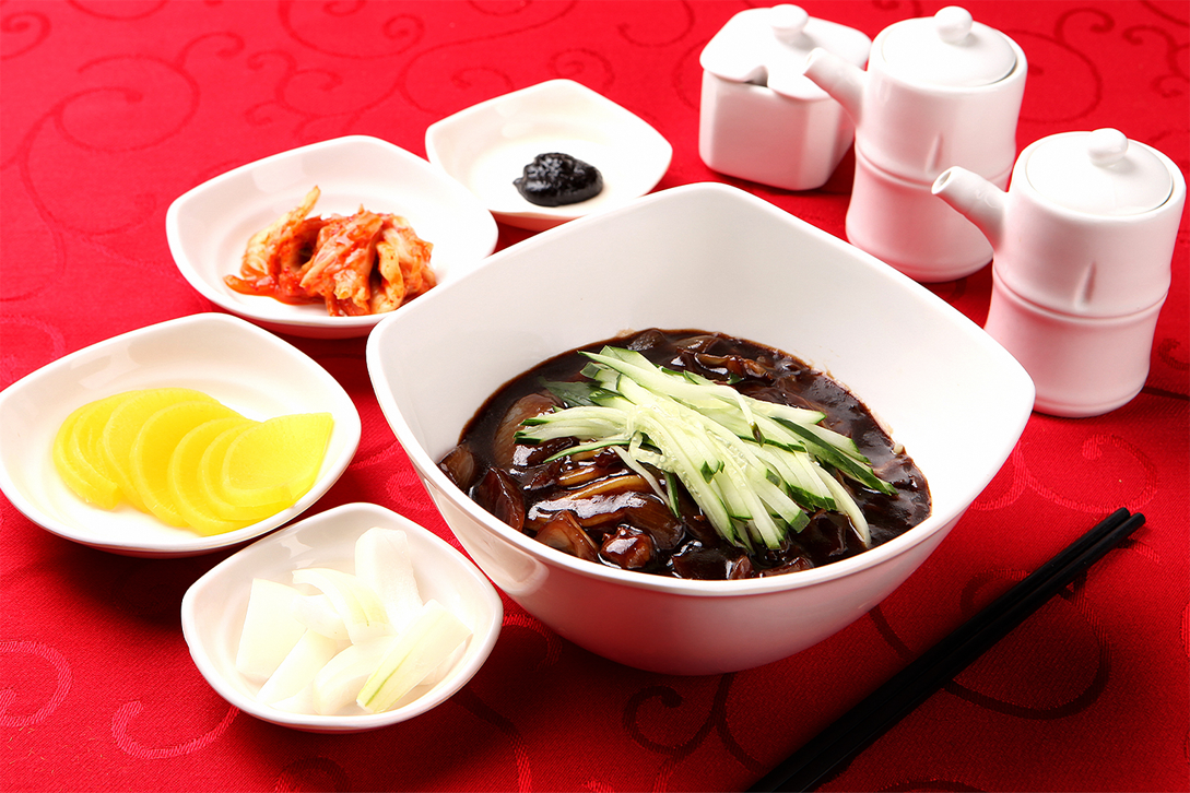 炸醬麵擺在紅色桌布上，配有泡菜和其他小菜，是韓國黑色情人節的代表性美食，為單身人士提供一種特殊的品味享受。