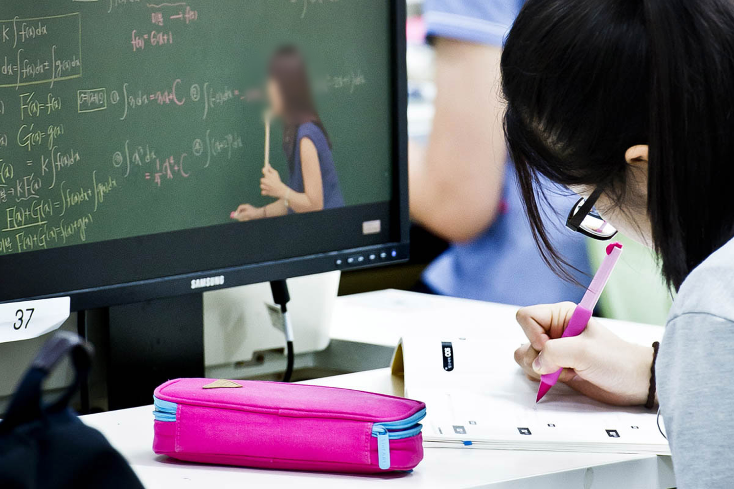 student studying at her desk watching online lecture with pink pen and pencilcase