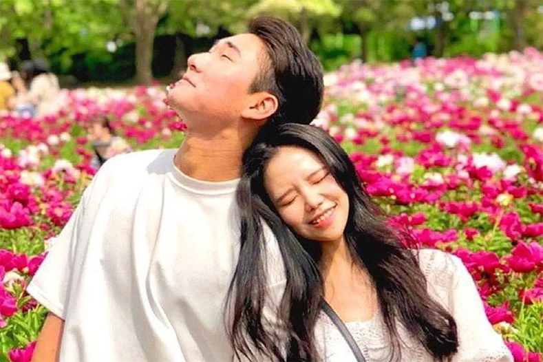 一對情侶在繁花景觀中，描述韓國用 '깨볶' 表示放閃的情況。