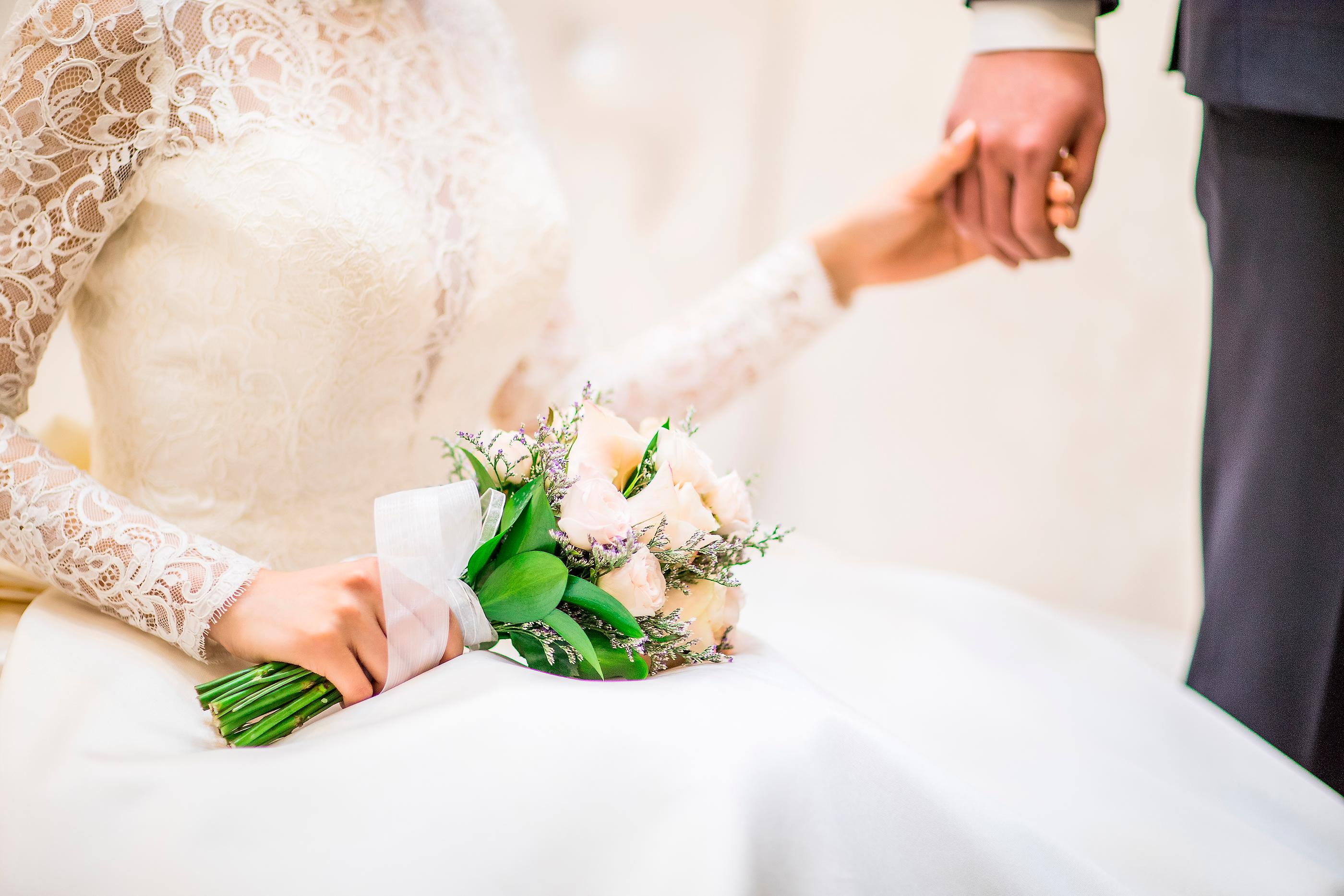 素敵な結婚式で新郎新婦が手を握り合い、花嫁が美しいブーケを持っている写真。