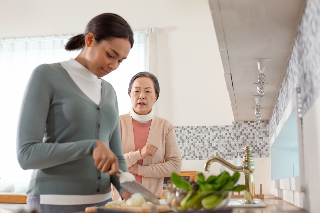 一位年輕女性在廚房切菜，另一位年長女性站在她後面觀看