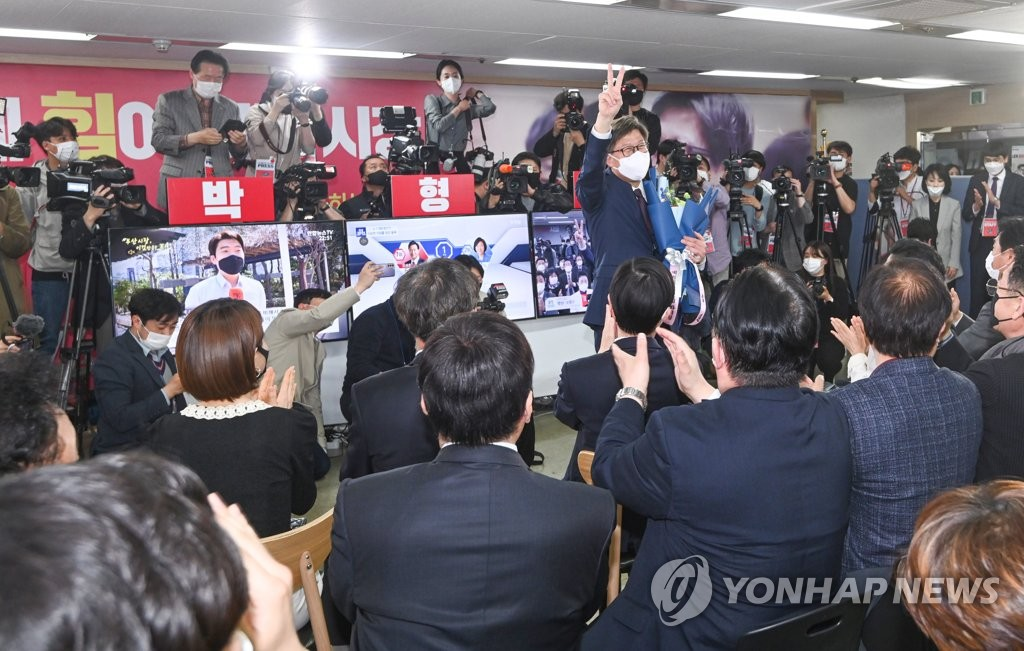 朴亨埈在釜山市长补选胜利后，手举胜利手势，周围是欢呼的支持者，象征国民力量党赢得釜山市长选举。