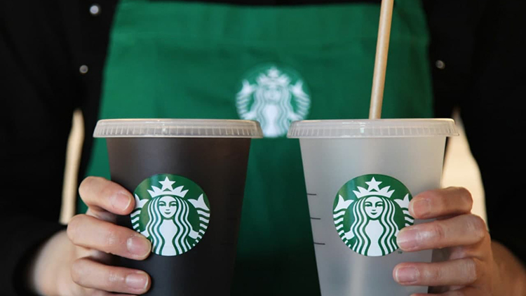 身穿星巴克围裙的工作人员展示两种不同颜色的星巴克杯子，体现环保与可重复使用的企业目标。