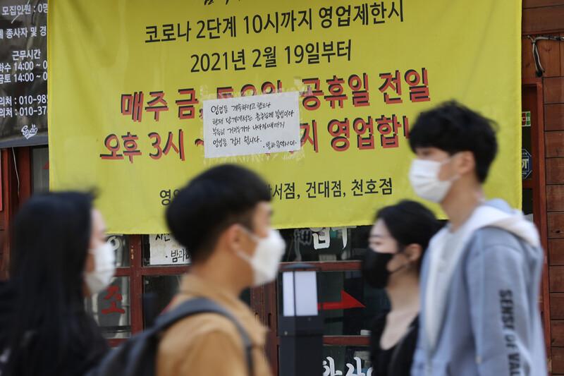 ソウルの弘大で営業中断の張り紙が貼られた店の前を通る人々。背景には営業時間に関連した注意書きが韓国語で書かれている。
