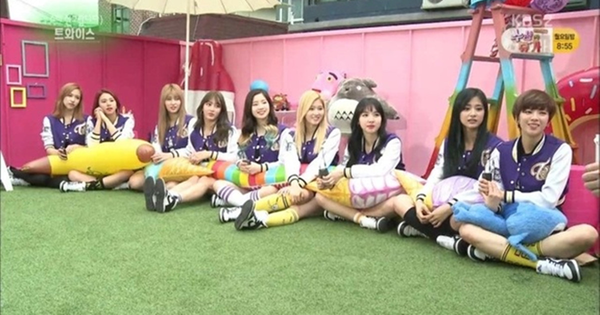 TWICE成員坐在草地上，圍在一起享受休閒時光。每個人都同樣盤腿坐著，呈現出韓國坐式文化的一部分，這種坐姿在韓國被稱為兩班腳。