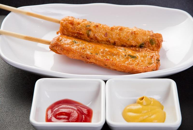 플레이트 위에 놓여있는 두개의 튀겨진 핫바, 케첩과 머스터드 소스가 옆에 놓여 있다.