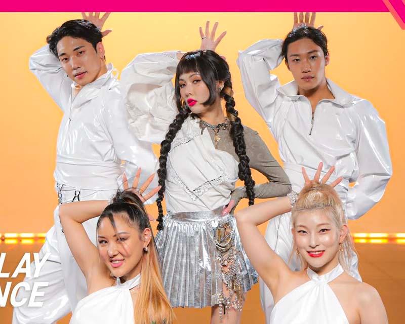 泫雅和舞者們身穿白色服裝在橙色背景下擺出充滿活力的舞台動作