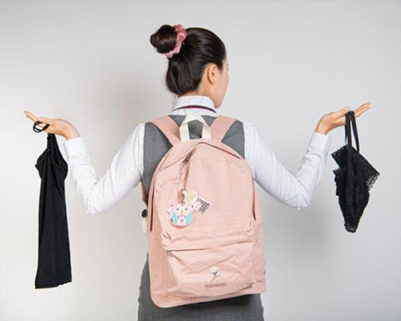 一名背著粉紅色書包的學生雙手攤開展示不同風格的內衣，象徵韓國學生對校服及內衣規定的困惑與質疑。