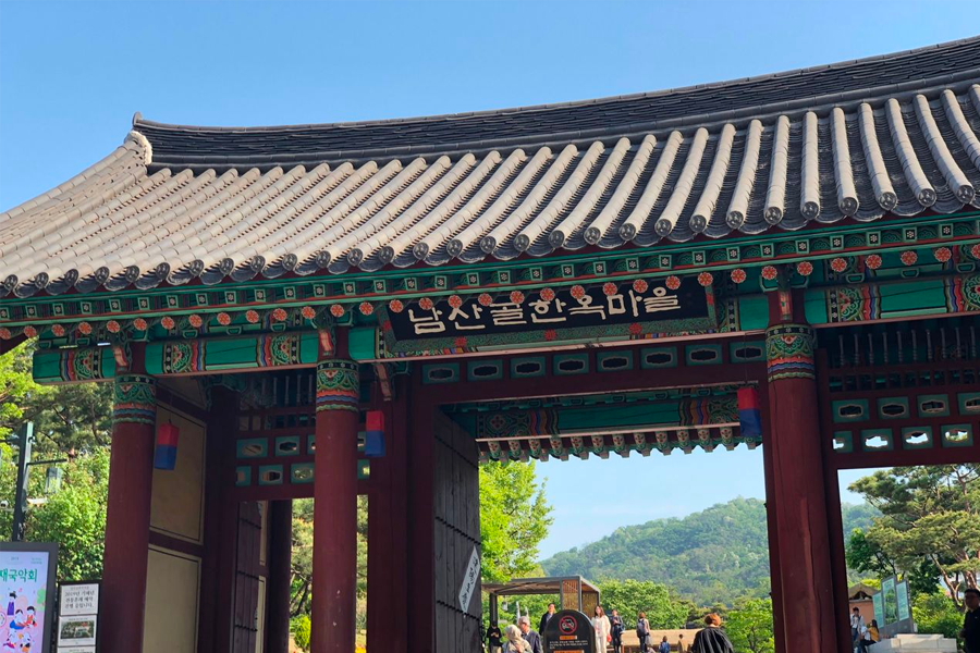 Traditional entrance gate of Namsan Valley Hanok Village, showcasing Korean architectural details and blue skies.